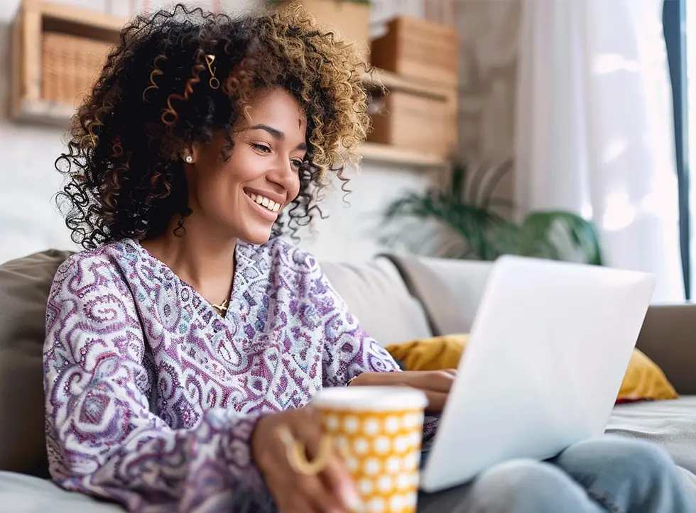 Woman on a sofa, happily looking at her laptop
